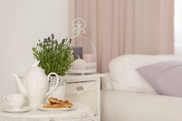 Close-up of kettle, dessert and lavender flowers on table in hotel bedroom interior with cabinet....