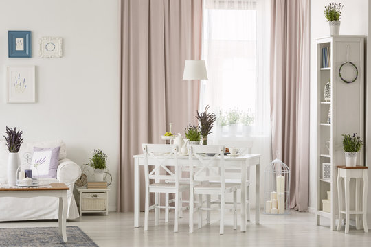 Lamp above table and chairs in white and pink apartment interior with posters and drapes. Real photo