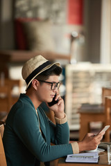Vietnamese young man talking on one phone and reading messages on another one