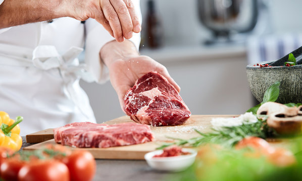 Chef Sprinkling Cooking Salt On A Raw Ribeye Steak