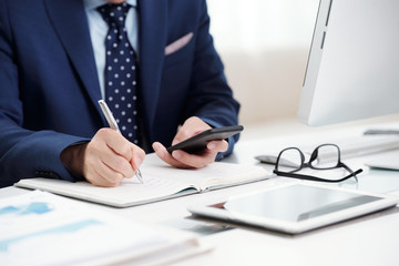 Cropped image of businessman checking messages in smartphone and taking notes in planner