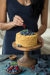 Woman decorates honey cake with fresh berry