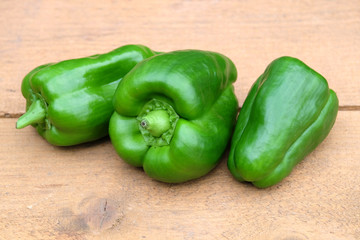 Still life with three appetizing whole green ripe bell peppers on brown wooden  surface close up