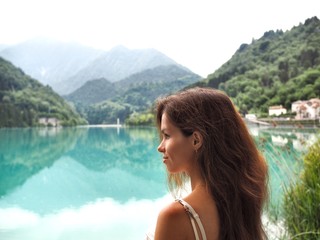 Obraz premium Profile of charming mysterious brunette girl with long hair on azure amazing mountain lake background.