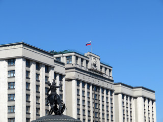 Parliament building in Moscow against clear blue sky. Russian flag on the State Duma, statue of St....