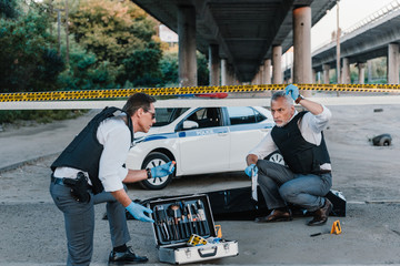 male police offier with clipboard talking to colleague in sunglasses near corpse in body bag at...