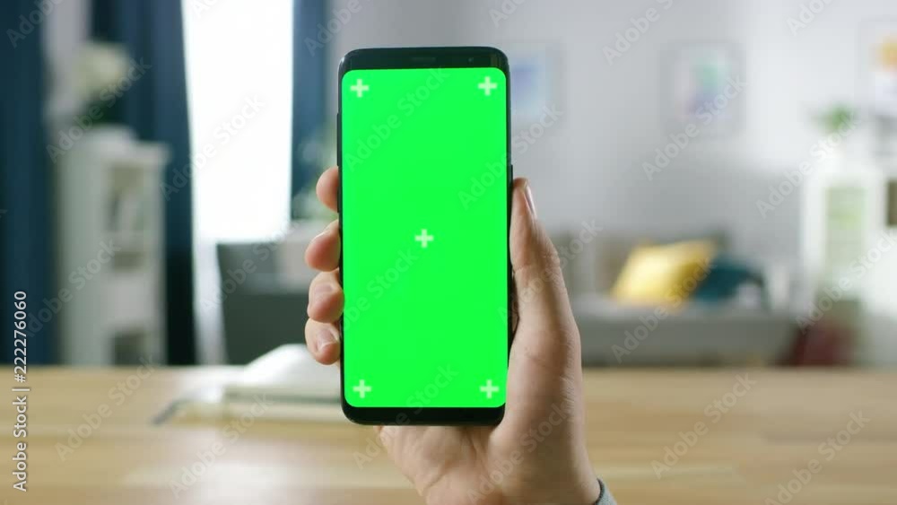 Poster close-up of a man holding green mock-up screen smartphone and using touchscreen gestures. touching m