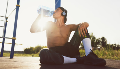 Horizontal image of fitness male drinking water out of plastic bottle after workout outdoor....