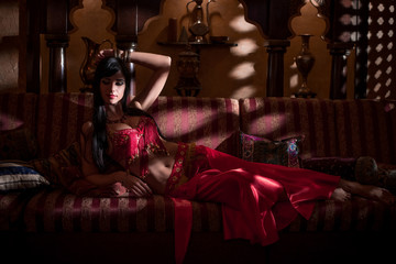 A girl in oriental attire in a dark room in the rays of light.