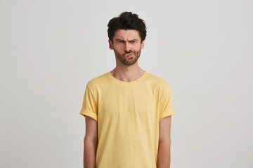 Closeup of sad dissatisfied young man with bristle wears yellow t shirt feels displeased and...