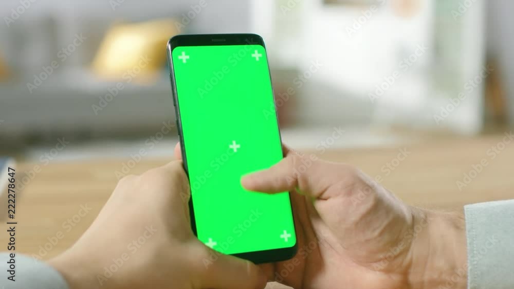 Poster close-up of a man uses green mock-up screen smartphone and does touchscreen gestures. touching mobil