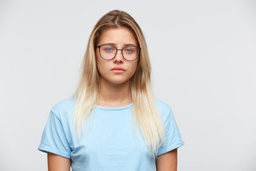 Closeup of sad upset young woman with blonde hair wears spectacles and blue t shirt feels depressed...