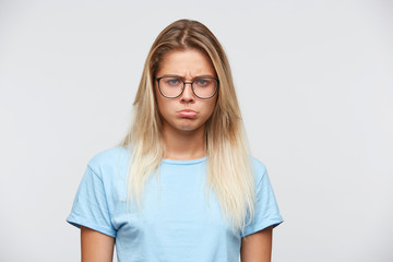 Portrait of unhappy disappointed young woman with blonde hair wears glasses and blue t shirt feels...