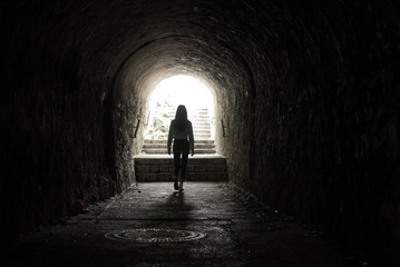 Girl walking throug dark tunnel into light