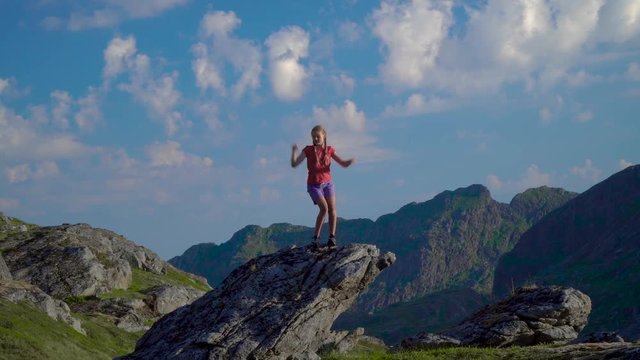 A teenage girl dances on a rock in the mountains of Norway. Crazy dancer girl having fun enjoying nature celebrating vacation travel in Lofoten island