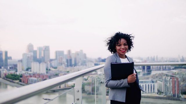A portrait of a businesswoman standing on a terrace, holding notes.