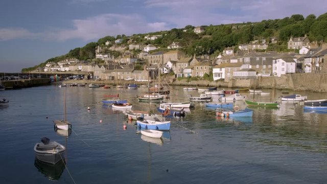 Camera rises from behind fence to reveal harbour of Mousehole in Cornwall
