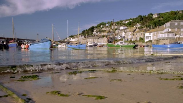 Low angle slide shot as waves break on beach in harbour of Mousehole in Cornwall