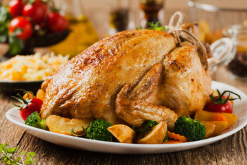 Roast chicken whole. Served on a plate with vegetables and baked potatoes.