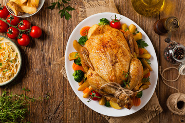 Roast chicken whole. Served on a plate with vegetables and baked potatoes.