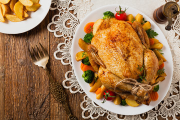 Roast chicken whole. Served on a plate with vegetables and baked potatoes.