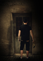 A young man with an ax stands in the night outside the door of the old house.
