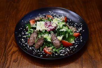 Sliced grilled beef steak with green leaves meat salad on black plate. Barbecue steak and healthy meat salad on wooden table. Come hungry, leave happy