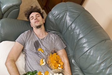 Tired young man sleeping on a sofa with food after party