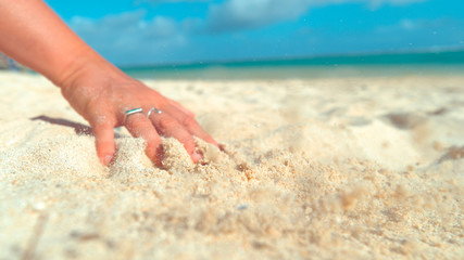 CLOSE UP: Playful young woman making a drawing in the sand with her fingers.