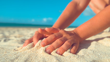 CLOSE UP: Unrecognizable girl playing on the beach gathering up a pile of sand.