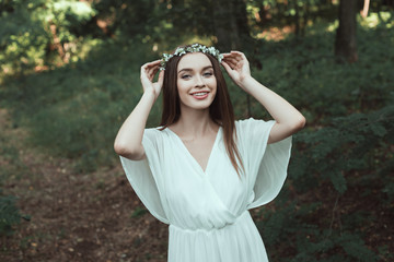 beautiful happy girl posing in floral wreath in forest