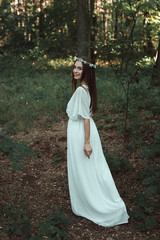 attractive smiling girl in white dress walking in forest