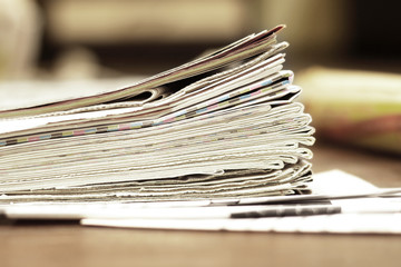 Pile of newspapers. Folded and stacked pages with news, headlines, articles and photos on the wooden table. Daily papers in the morning. Selective focus, blurred background  