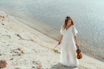 Fototapeta na wymiar attractive girl in white dress holding violin on seashore