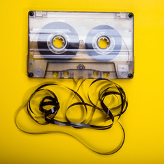 Old audio cassette with a tangled magnetic tape on a yellow background.
