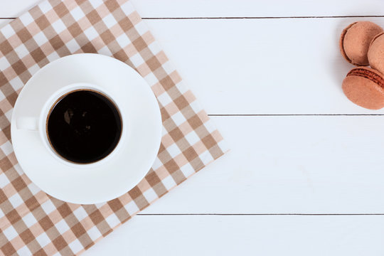Cup of coffee with macaroons on napkin and white background. Top view, copy space.