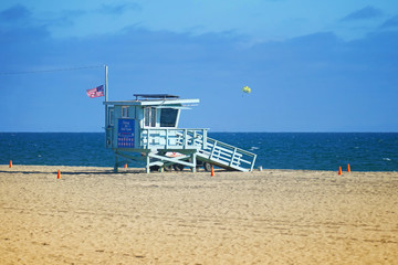 Obraz premium Lifeguard tower on a sandy beach, with kite surfer in the background, Santa Monica, California