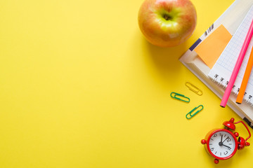 Stationery, Apple and clock on yellow table with copy space. Education concept, school and office.