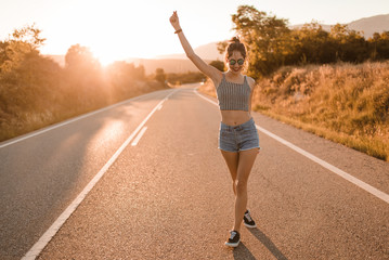Young girl with hair bun and denim shorts dancing walking and smiling on the edge of the roadway in a sunset of summer