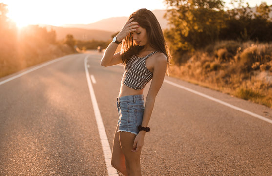 Young girl with hair bun and denim shorts dancing walking and smiling on the edge of the roadway in a sunset of summer