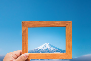 hand hold wood frame and focus Fuji mountain on background. image look like photo on the frame. nature wallpaper and background. 