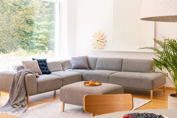 Golden tray with croissants on a gray ottoman and a creative, wooden clock in a sunlit living room...
