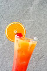 Tequila sunrise cocktail in glass on gray stone