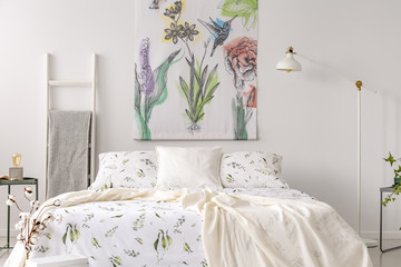 A pastel bedroom interior with a bed dressed in green plants pattern white linen. Fabric painted in flowers and birds on the background wall. Real photo.