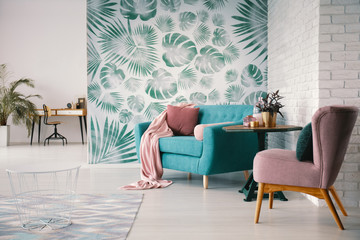 Chair and turquoise sofa in green living room interior with leaves wallpaper and table. Real photo - obrazy, fototapety, plakaty