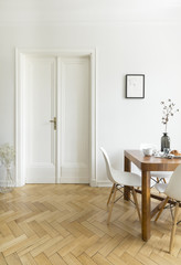 A bright dining room interior with a wooden table and chairs standing on a herringbone parquet...