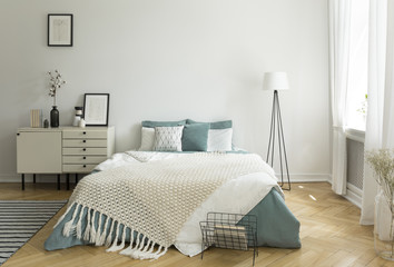 A big comfortable bed with pale sage green and white linen, pillows and blanket in a woman's bright bedroom interior with windows. Real photo. - obrazy, fototapety, plakaty