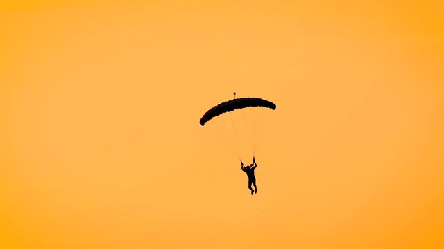 Silhouette of a man paragliding on parachute in yellow sky, fiery sky during sunset.