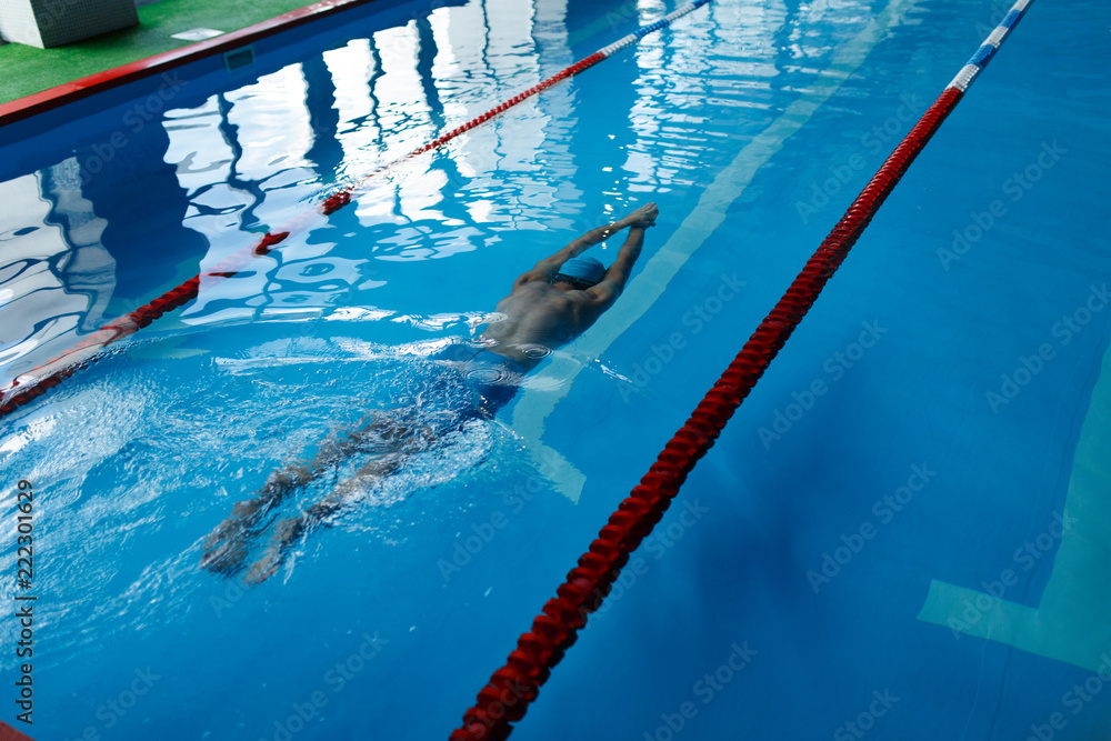 Wall mural photo on top of athlete man in blue cap swimming on path in pool under water