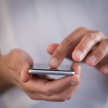 Squared image of young caucasian man using apps on a touchscreen smartphone - Hands close-up focus on phone - Concept for using technology, shopping online, using mobile apps, texting, phone addiction